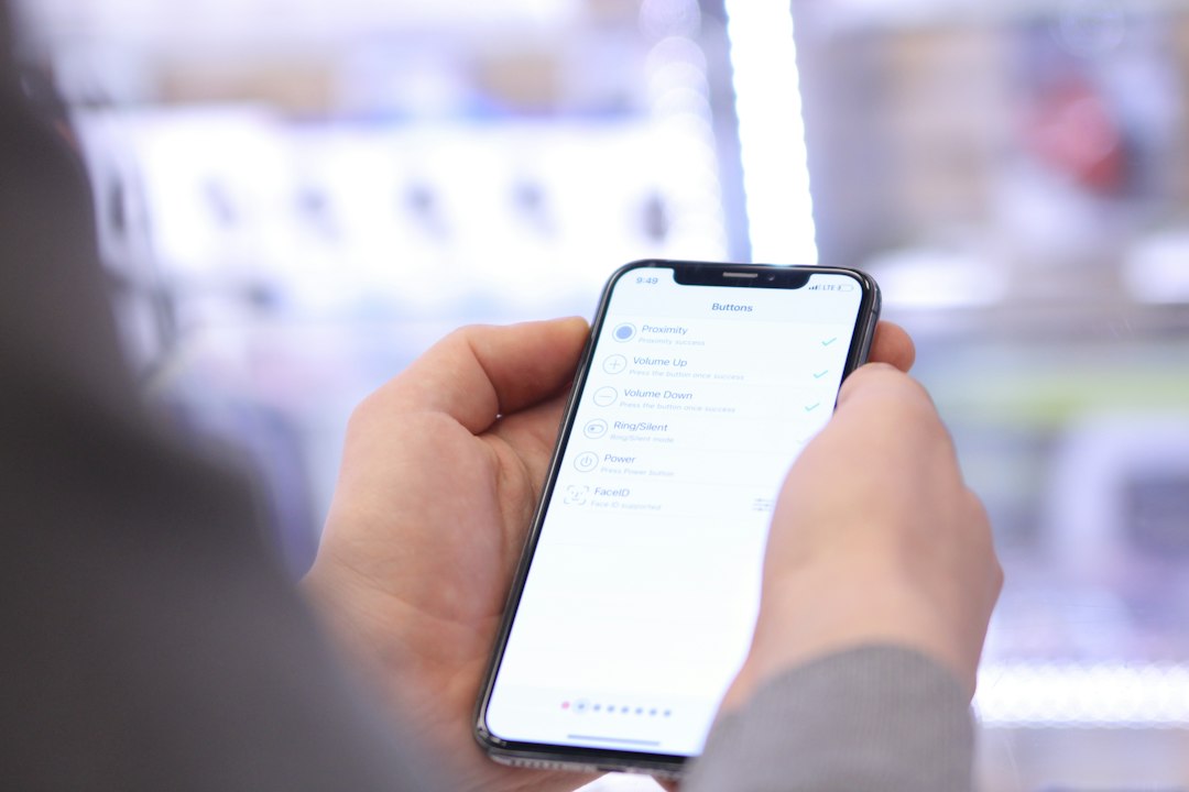 Close-up of hands holding a smartphone showing a list of button actions (Buttons) such as Proximity, Volume Up, Volume Down, Ring/Silent, Power, Face ID, with a blurred store background.