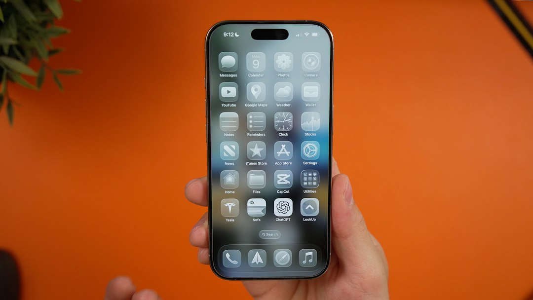 Hand holding a smartphone showing a dense grid of app icons on the home screen against an orange background.