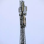 Cell tower with multiple antenna panels against a clear blue sky.
