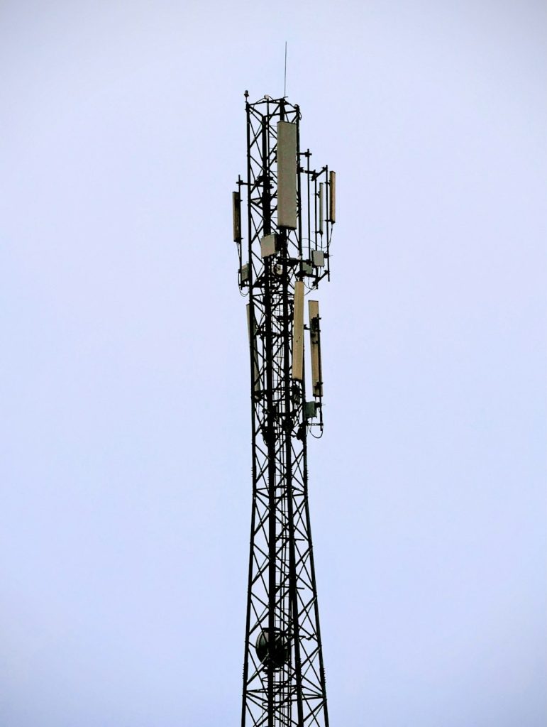 Cell tower with multiple antenna panels against a clear blue sky.