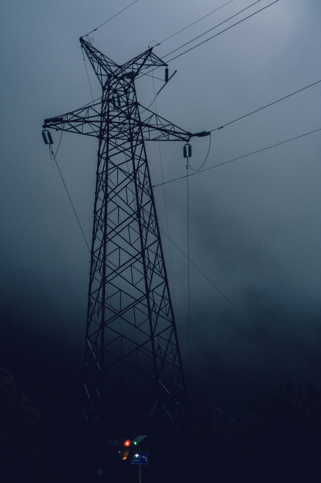 High-voltage transmission tower with multiple wires against a dark, foggy sky; power lines extend into the distance.