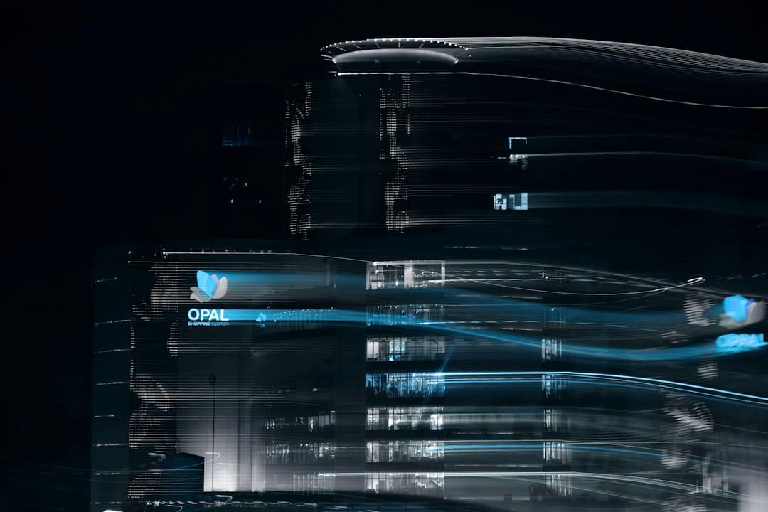 Nighttime cityscape with blurred blue light trails around a glass building and OPAL Shopping Center signage.