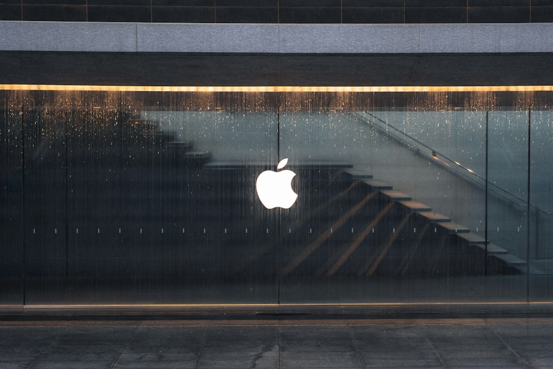 Apple logo illuminated on a rain-splashed glass storefront, with diagonal interior stairs visible behind the window.