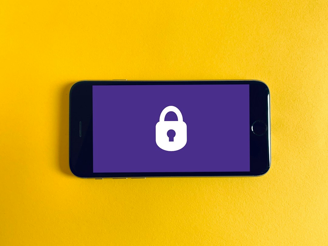 Smartphone on a yellow surface showing a white padlock icon on a purple screen, signaling security (locked screen).