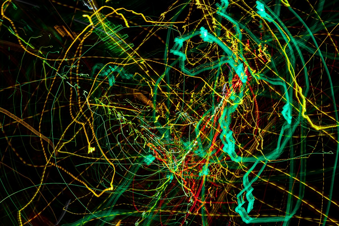Abstract composition of neon green, turquoise, and yellow light trails crossing over a dark background.