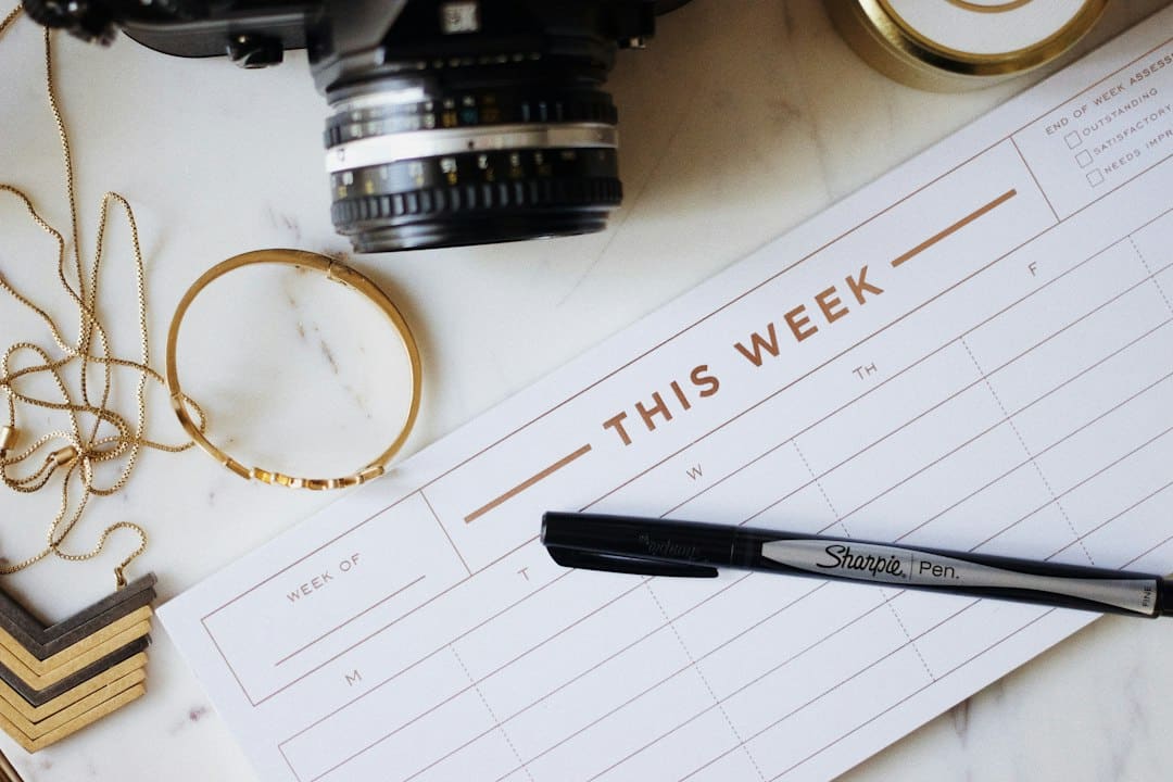 A camera, jewelry, and a weekly planner on a marble surface, with a Sharpie pen ready to write.