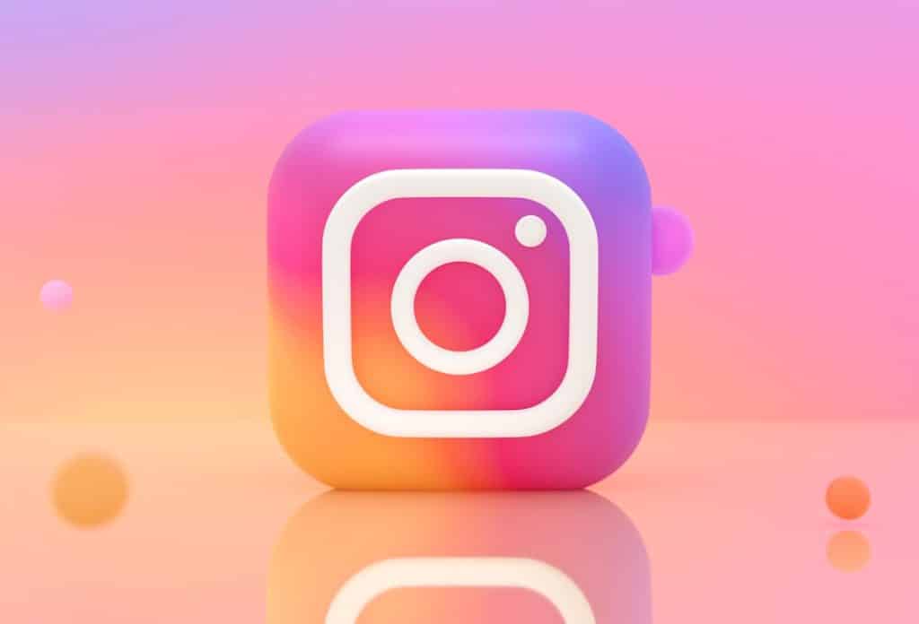 3D Instagram logo cube with the camera glyph on a pink–orange pastel gradient background with reflections