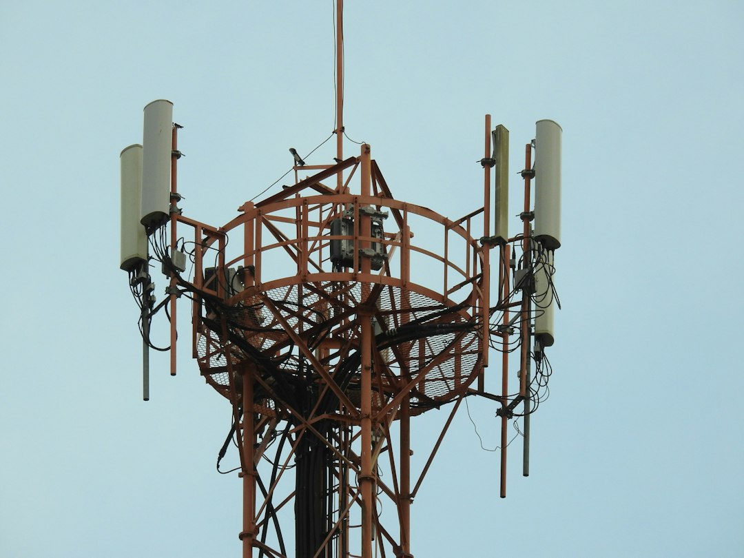 Cellular antenna tower with multiple white panel antennas against a clear blue sky.
