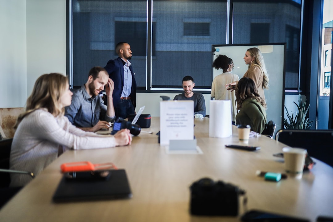 A diverse group of coworkers seated and standing around a long conference table in a modern office during a meeting.