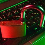 Padlock on a laptop keyboard bathed in red and green light, symbolizing cybersecurity and data protection.