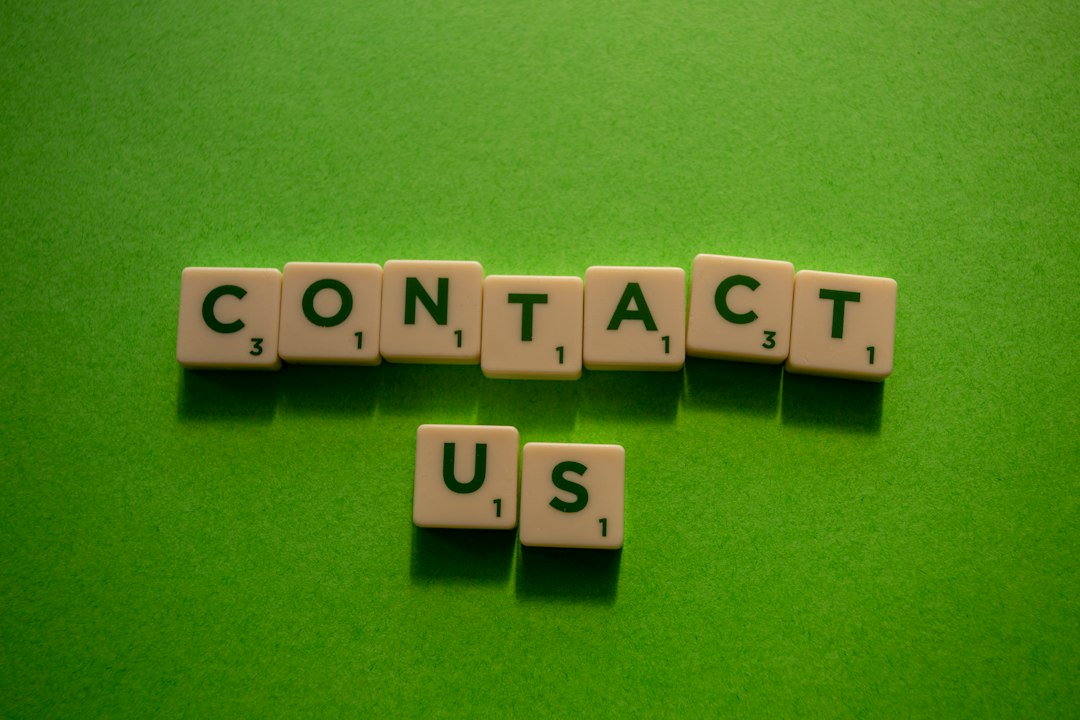 Scrabble tiles spell 'CONTACT' on a bright green surface, with 'US' placed below the word.