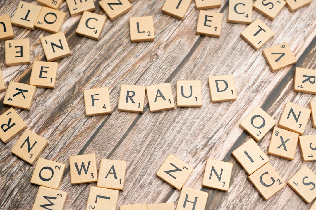 Scrabble tiles on a wooden surface spelling the word FRAUD.