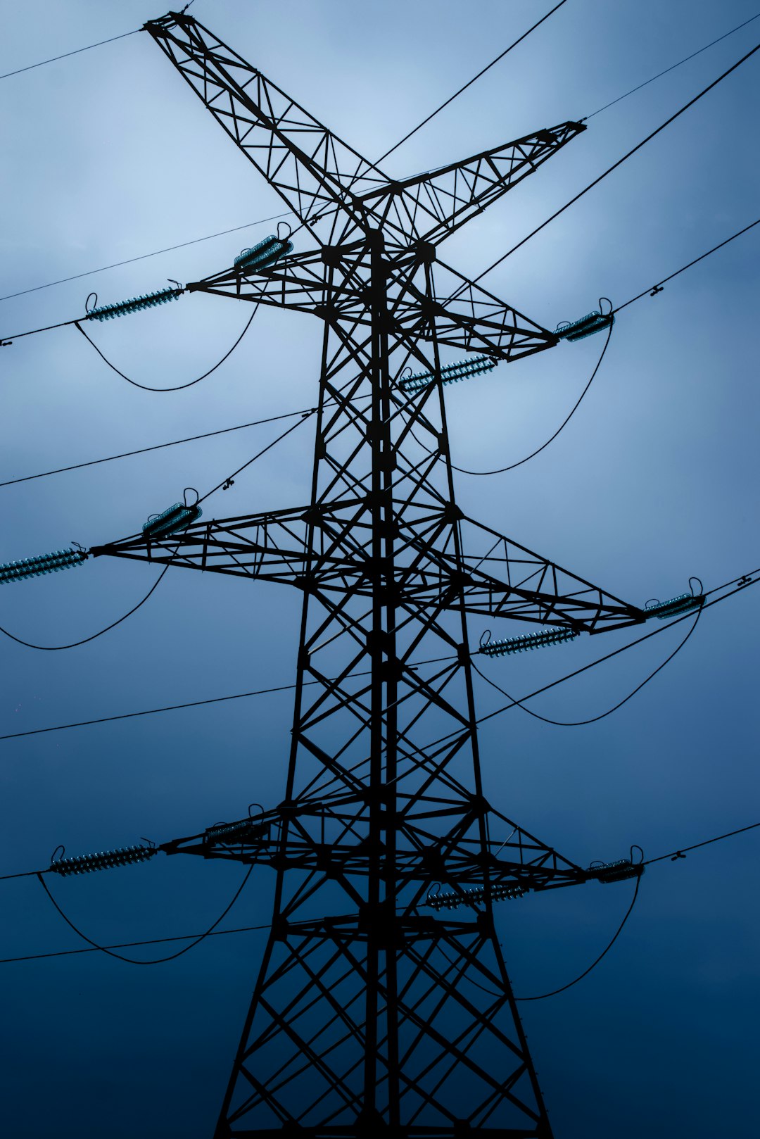 Silhouette of a high-voltage transmission tower with power lines against a blue sky.