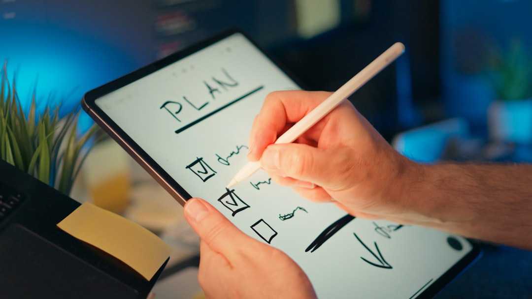 Person holds a tablet and writes a plan with a stylus, checking off a to-do list on screen.