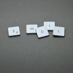 Tiles spell 'EMAIL' on a gray surface using white square letter tiles with black letters and a euro symbol on the first tile?