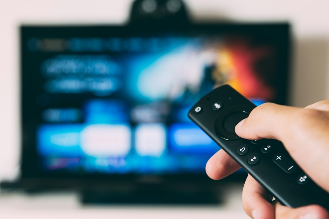 Person holding a TV remote aimed at a blurred television screen, ready to change the channel or adjust volume