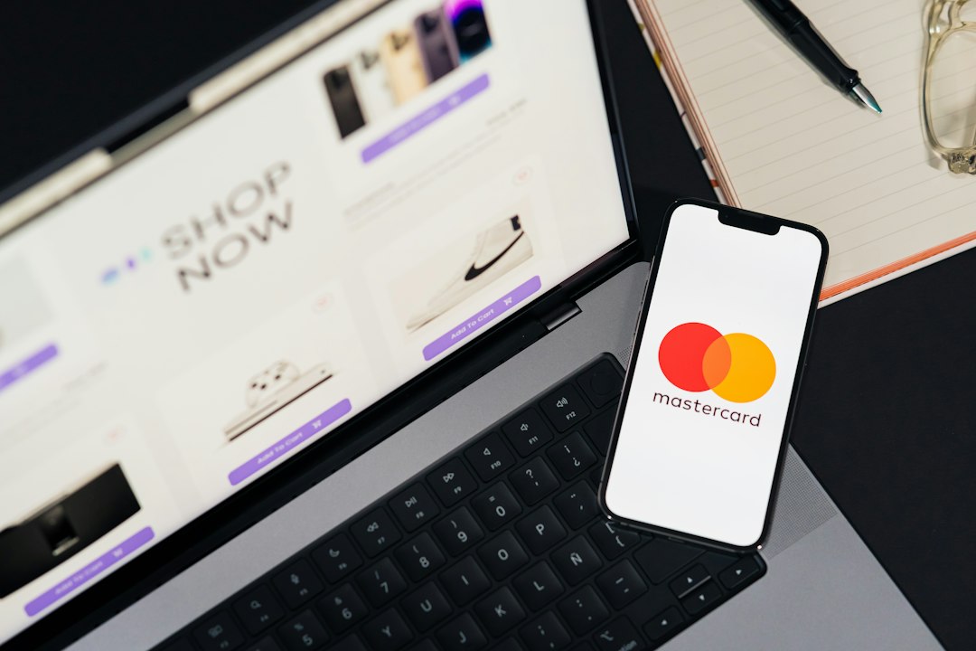 Open laptop shows an online shop page; a smartphone on the keyboard displays the MasterCard logo, suggesting online payments.