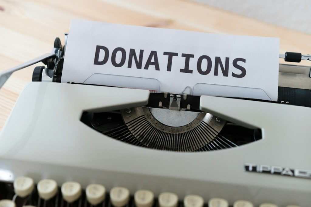 Vintage typewriter with a sheet reading DONATIONS on a wooden desk surface.