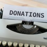 Vintage typewriter with a sheet reading DONATIONS on a wooden desk surface.