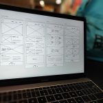 Open MacBook displaying a grid of hand-drawn website wireframes on the screen, showing four columns labeled Landing Page, Our Product, About, News.