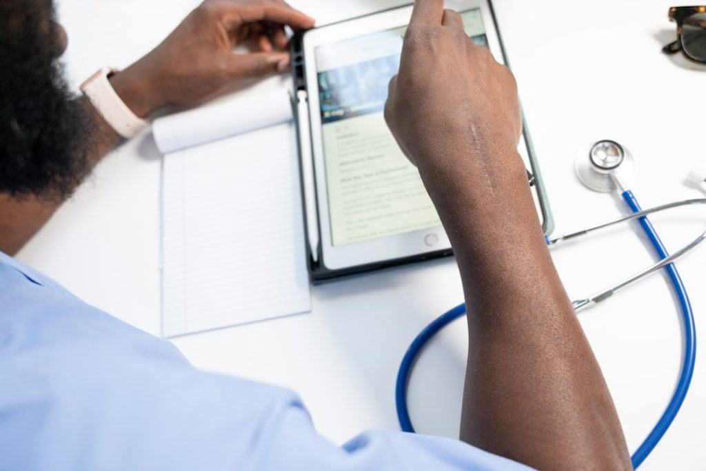 Healthcare professional reading medical notes on a tablet at a clean desk, with a stethoscope nearby.
