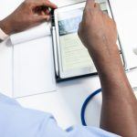 Healthcare professional reading medical notes on a tablet at a clean desk, with a stethoscope nearby.
