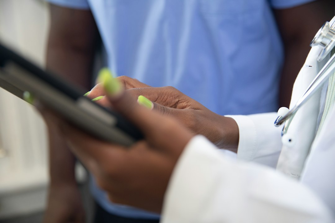 Two healthcare professionals review information on a tablet, one in a white coat with a stethoscope nearby.