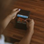 Person’s hands hold a brown leather wallet on a wooden table, exposing several cards in the card slots.