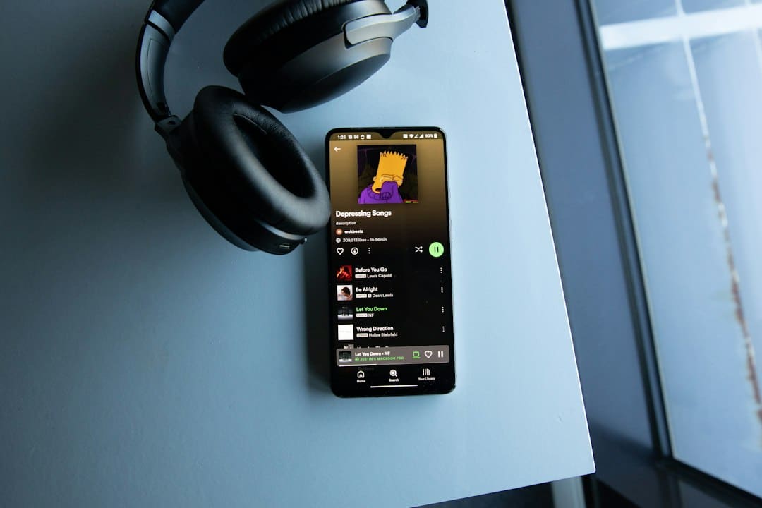 Smartphone playing Spotify with Simpsons album art, resting on a desk under a pair of over-ear headphones.