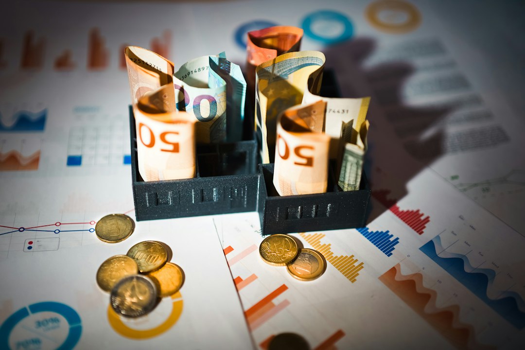 Tray of rolled euro banknotes and coins on top of financial charts and graphs, suggesting budgeting or investment planning