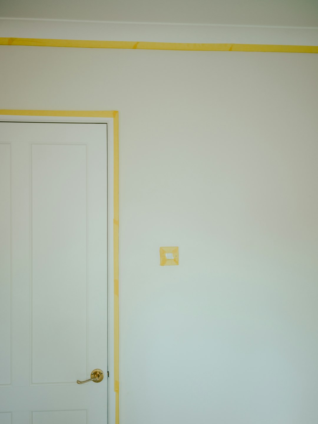 White interior door on the left with yellow painter’s tape along the frame and around the light switch on the wall