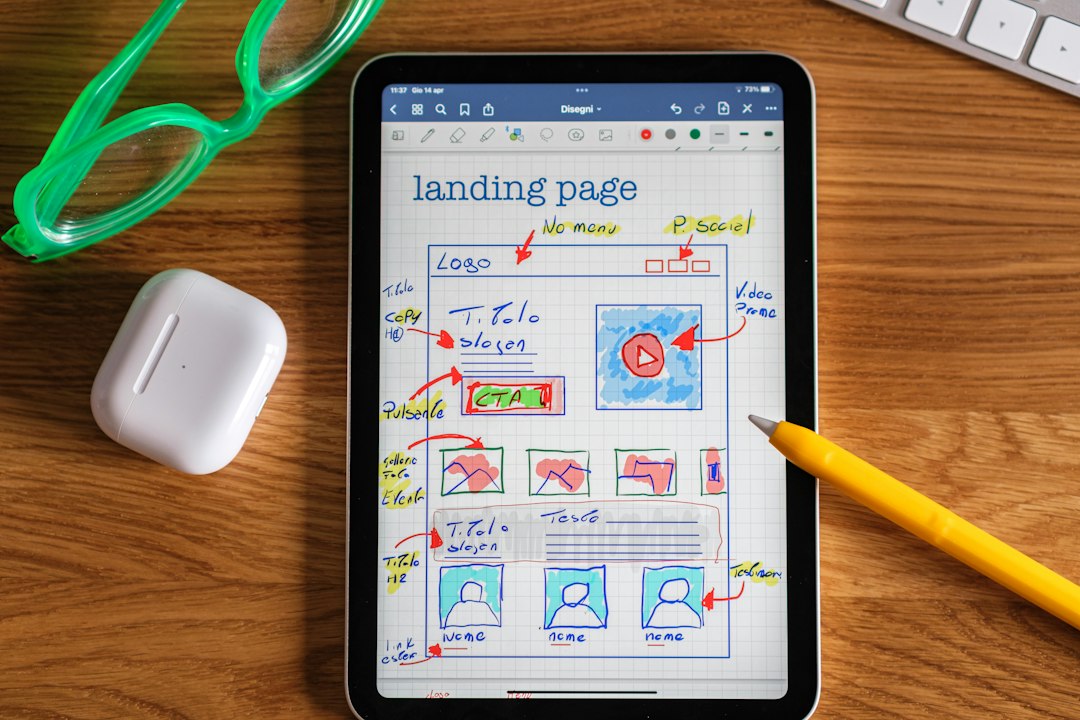 Tablet on a wooden desk showing a hand-drawn wireframe sketch of a landing page on grid paper, with labels like Logo, Slogan, CTA, and video placeholder, plus small thumbnails and user avatars nearby.