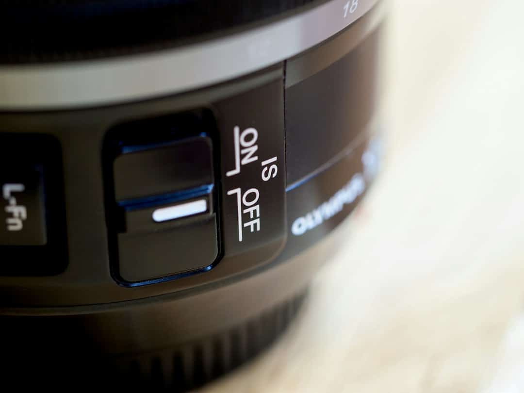 Close-up of a camera's IS switch labeled ON/OFF on a black body, with a white highlight visible