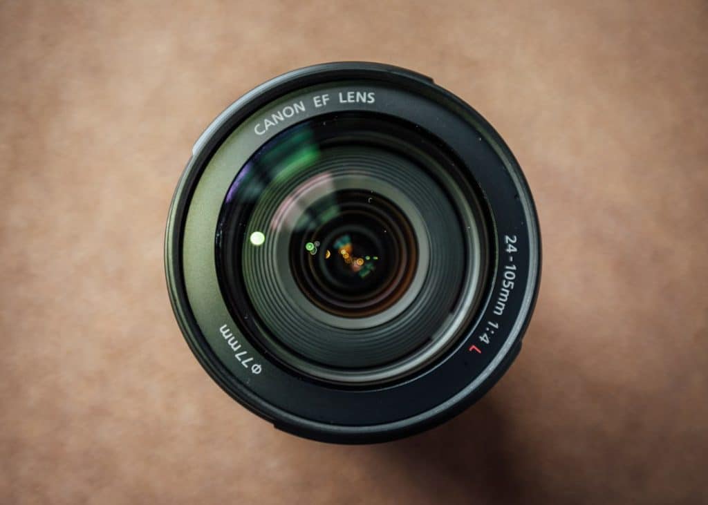 Top-down view of a Canon EF lens, 24-105mm, sits on a brown surface, glass elements reflecting light