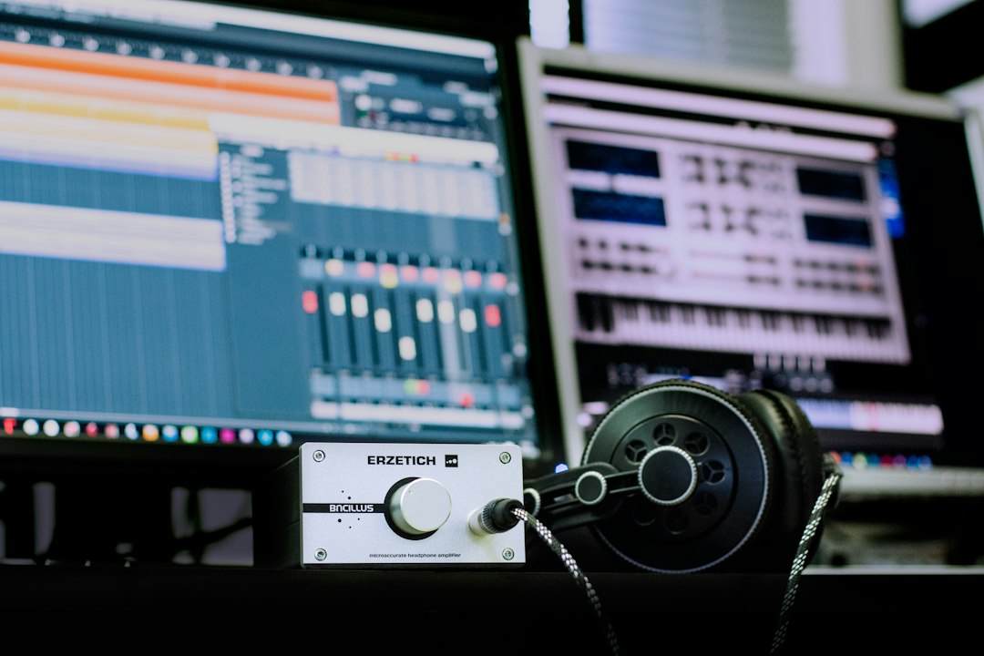 Studio desk with an Erzetich headphone amplifier and black over-ear headphones; two monitors show a DAW and a synth in the background.