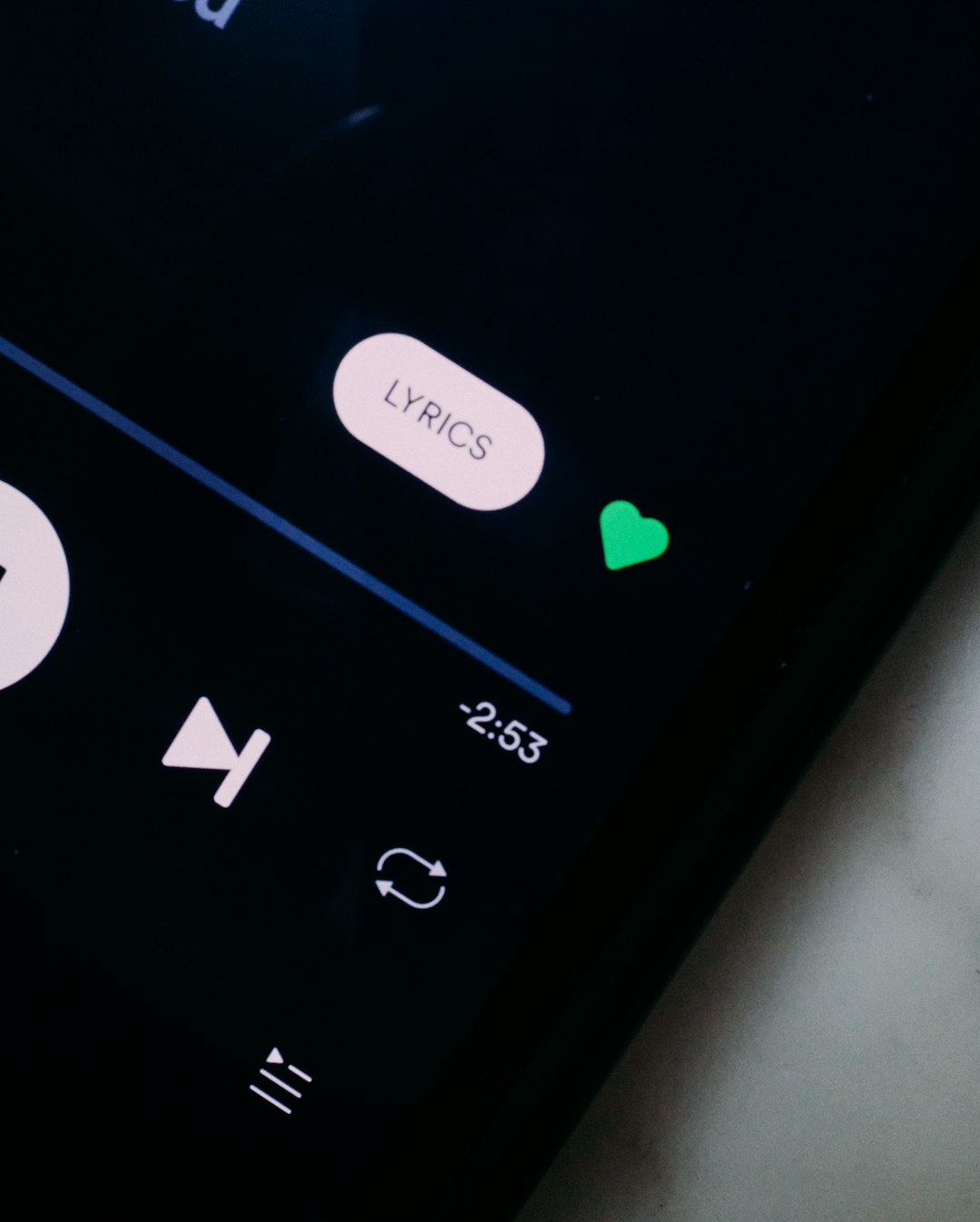 Close-up of a phone screen showing a rounded white 'LYRICS' button, a green heart, and a progress time of -2:53 on a dark background.
