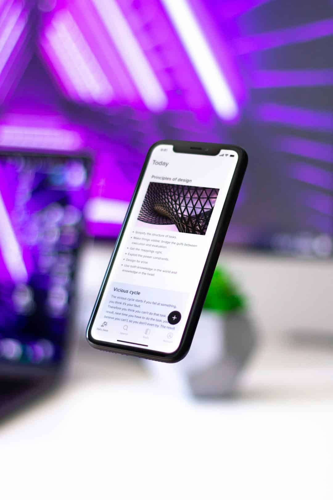 Smartphone floating in a purple-lit background, screen shows an article titled 'Principles of design' with text and image thumbnail.