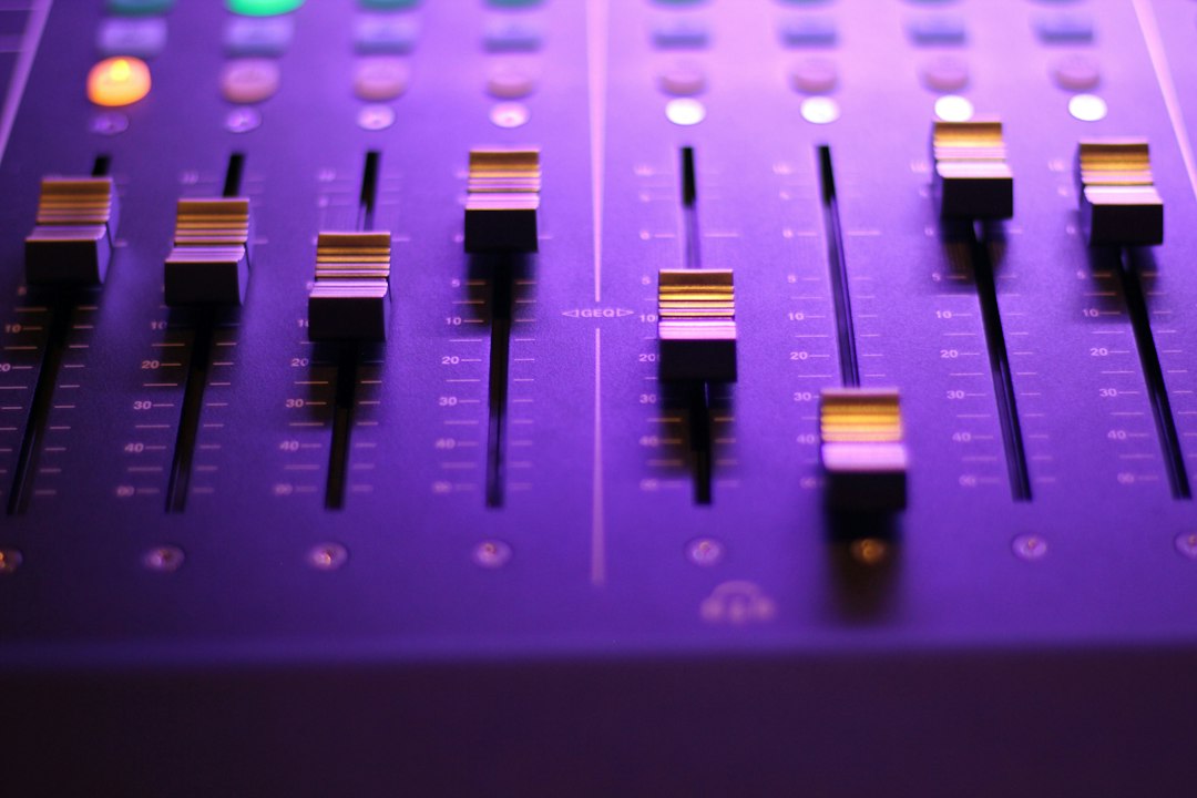 Close-up of a music mixing board with vertical faders and stacked sliders under purple lighting.