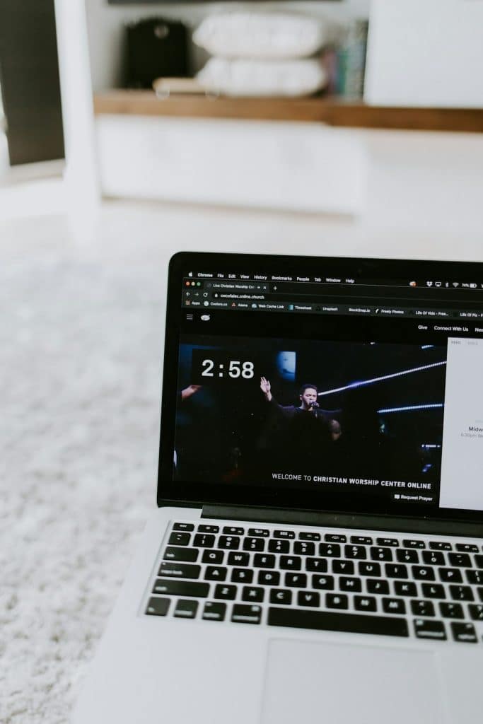 Laptop screen displaying a church online service with a speaker on stage and a 2:58 countdown.