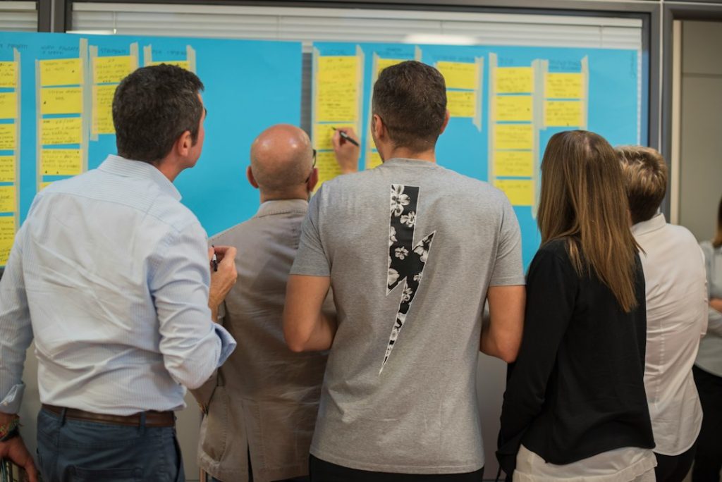 Group of people standing in front of a blue board covered with yellow sticky notes during a brainstorming session