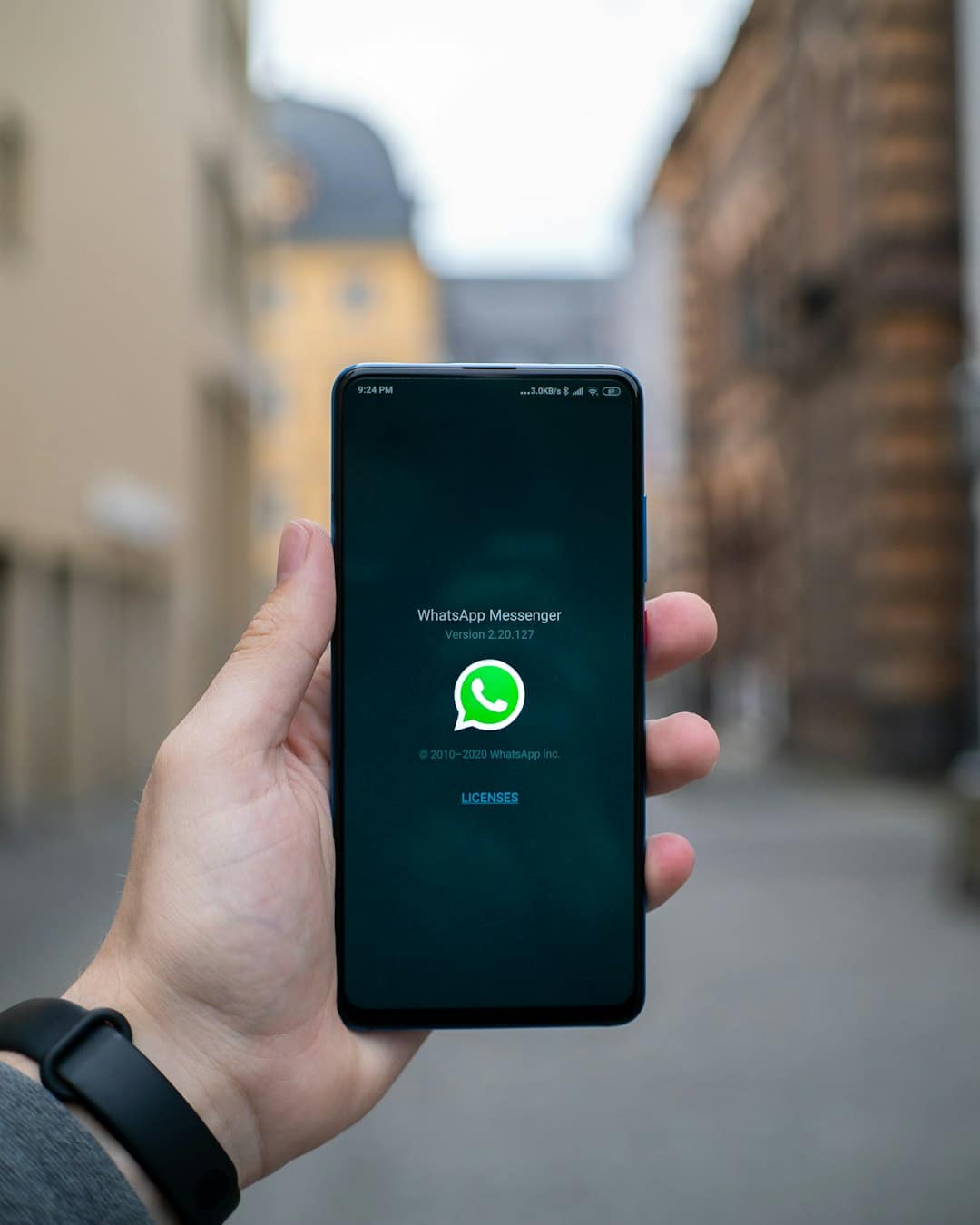 Hand holding a smartphone outdoors showing the WhatsApp Messenger startup screen with the green logo in the center.