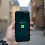 Hand holding a smartphone outdoors showing the WhatsApp Messenger startup screen with the logo visible.