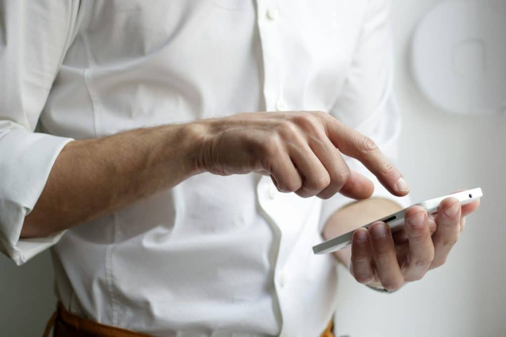 Person in a white shirt taps on a white smartphone held in one hand.