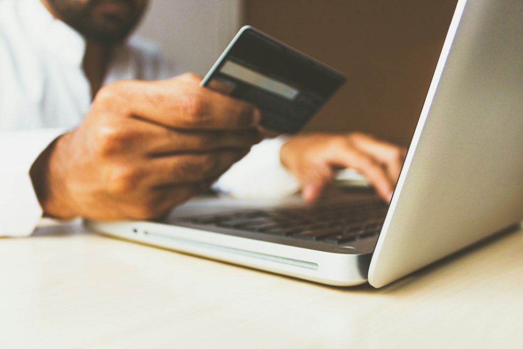 Person holding a credit card while typing on a laptop, suggesting online checkout