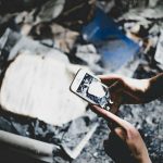 Person holding a smartphone and taking a photo of rubble and debris on the ground.