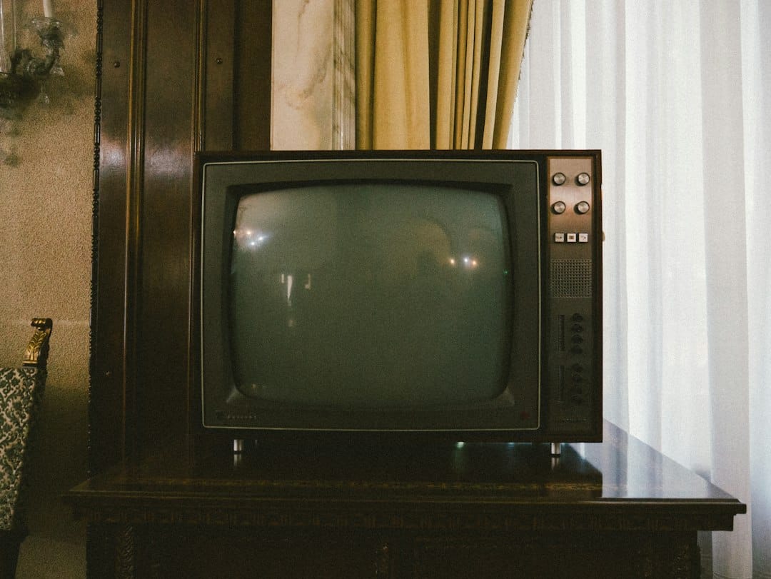 Vintage CRT television on a dark wooden stand in a classic living room with striped curtains and patterned furniture nearby.