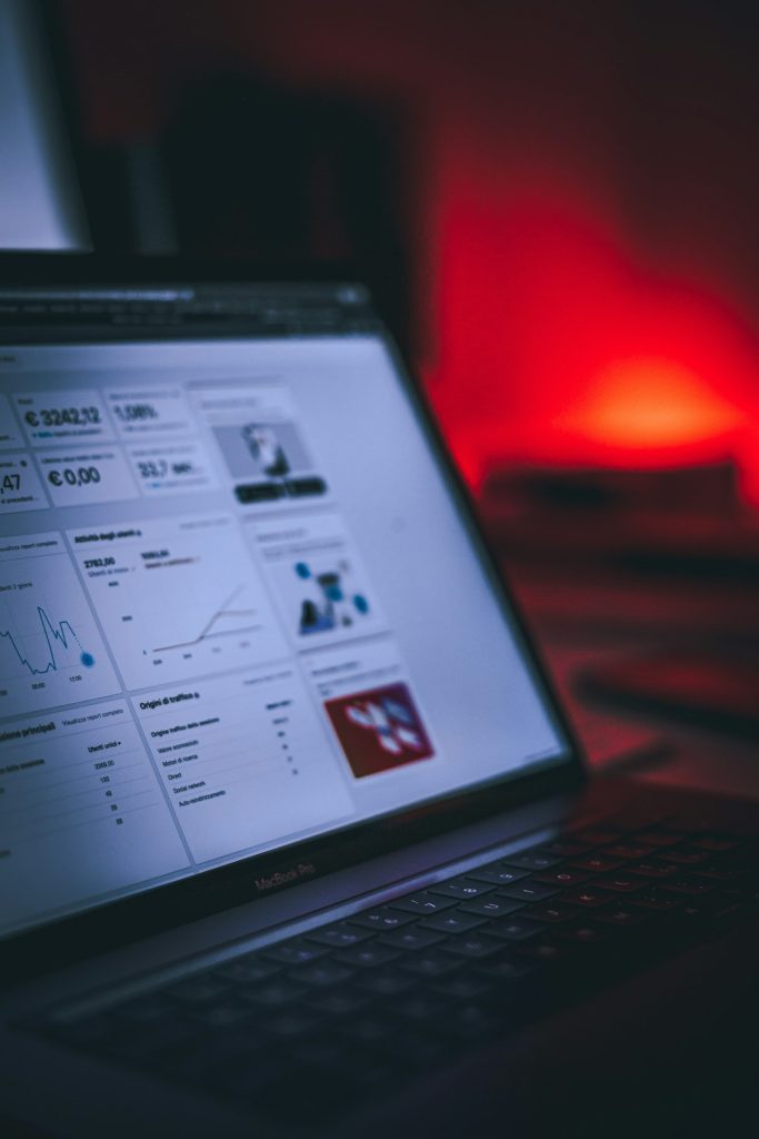 Open laptop showing a multi-panel analytics dashboard with charts, lit by a red ambient glow in a dark room.