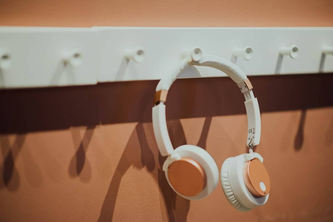 White over-ear headphones with copper accents hanging on wall hooks beneath a white power strip.