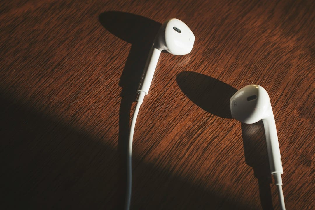 White wired earbuds resting on a dark wooden table, with pronounced shadows across the surface.