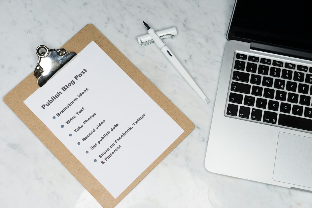 Clipboard with a checklist titled 'Publish Blog Post' listing steps like brainstorm ideas, write text, take photos, record video, set publish date, and share on social media, on a marble desk next to a pen and laptop.